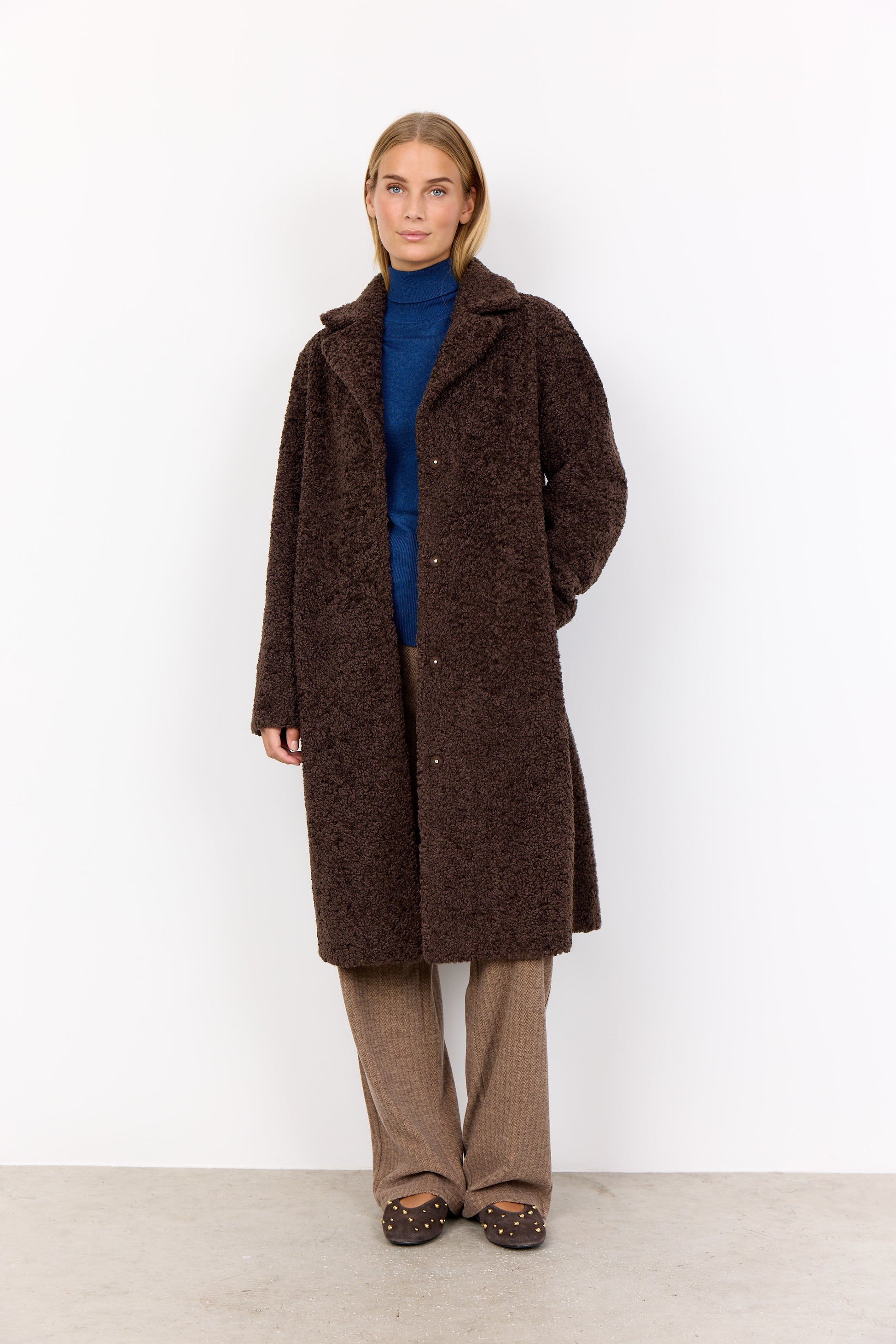 Person wearing a brown coat standing against a white background