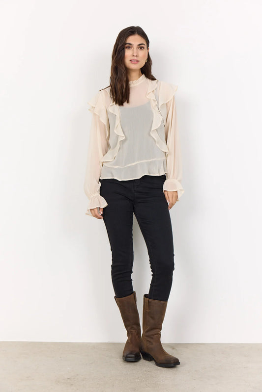 Woman wearing a cream blouse and black trousers and brown boots with a white background