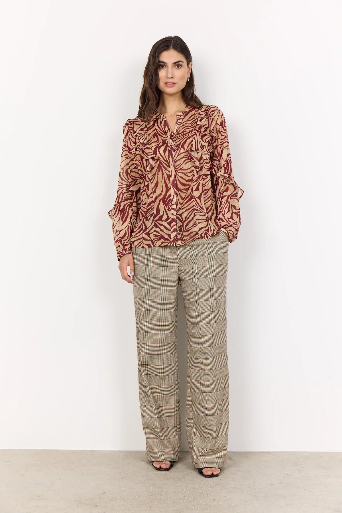 Woman wearing a patterned blouse and beige pants against a white background