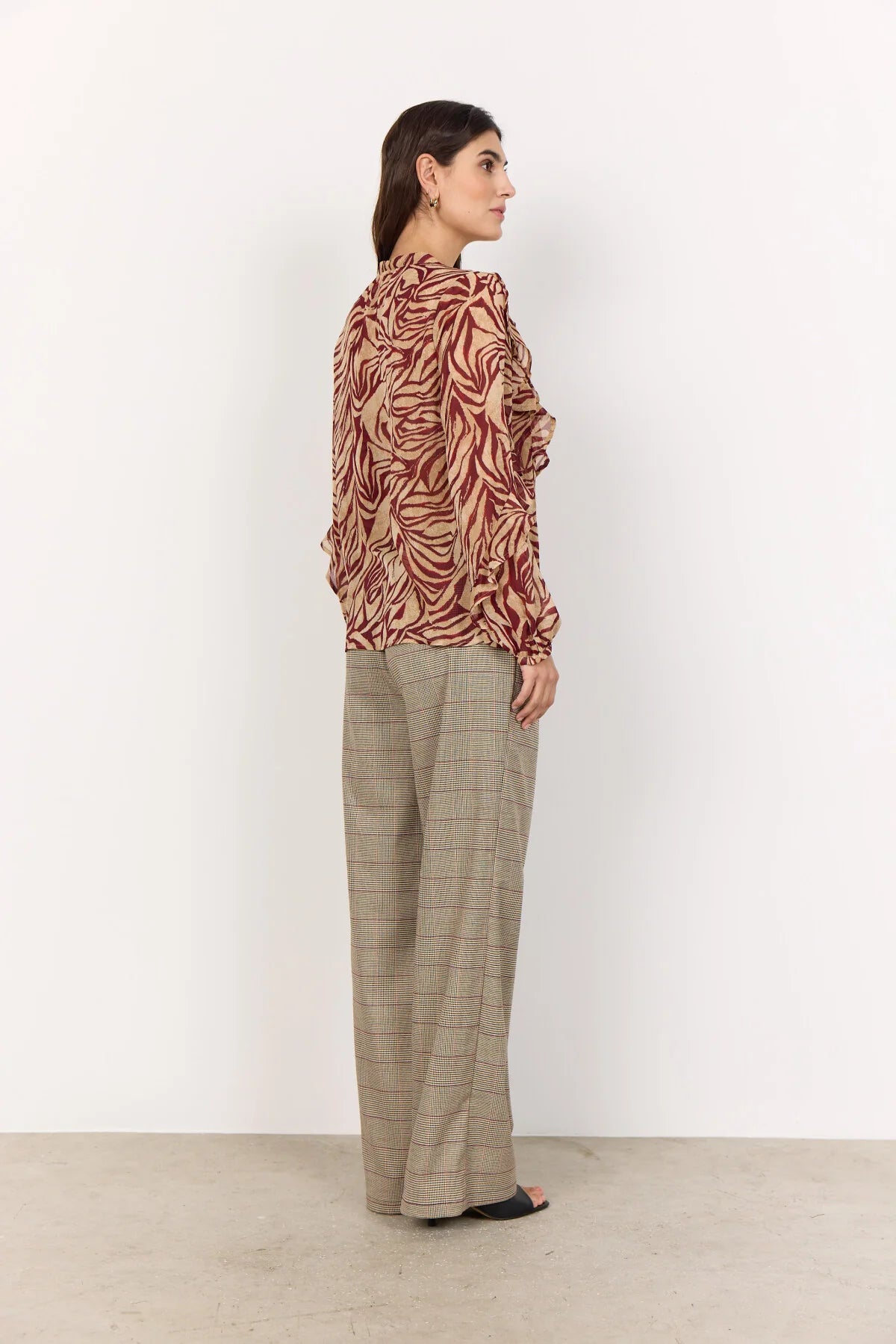 Woman wearing a patterned blouse and checkered pants against a white background