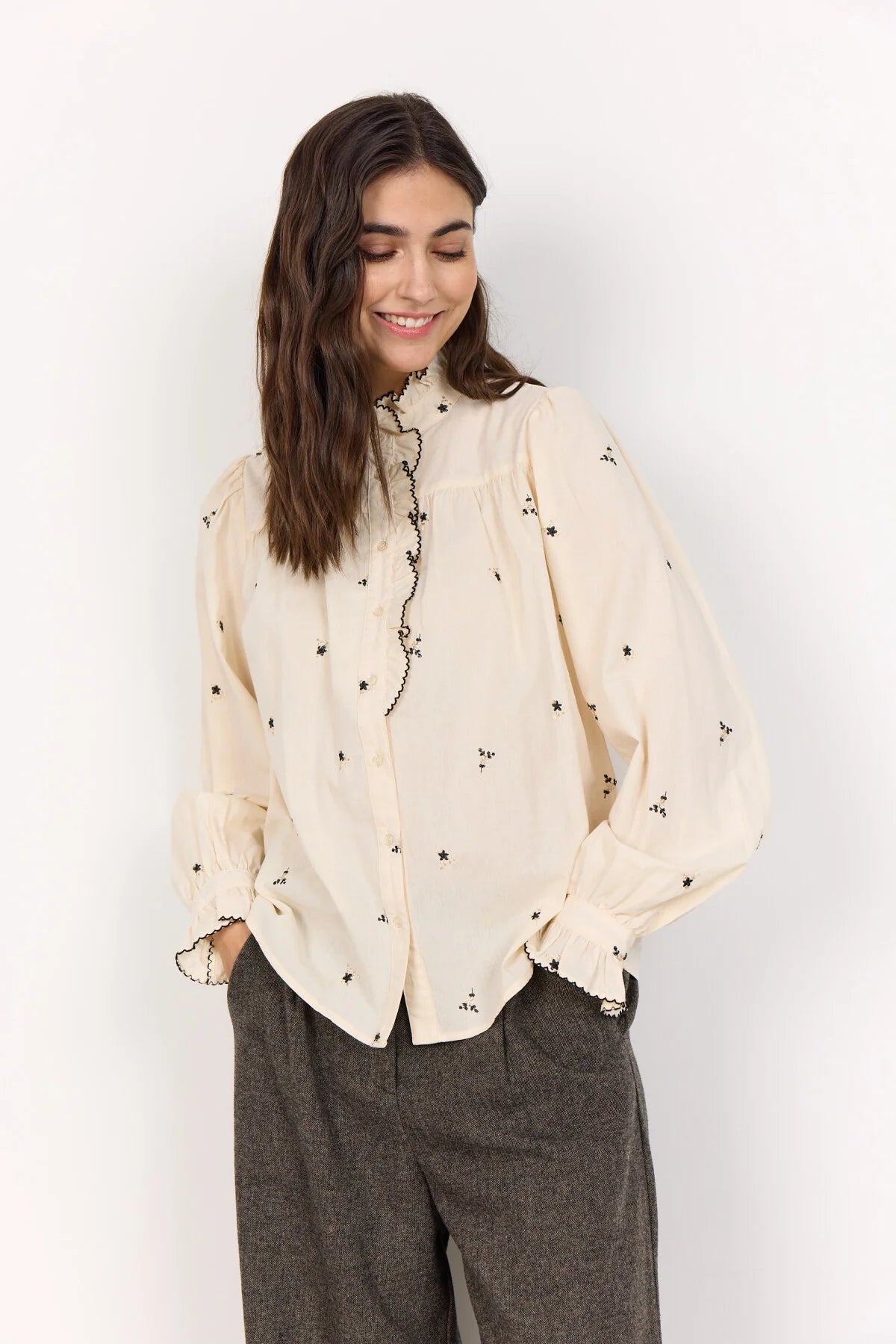 Woman wearing a beige blouse with black floral patterns against a white background