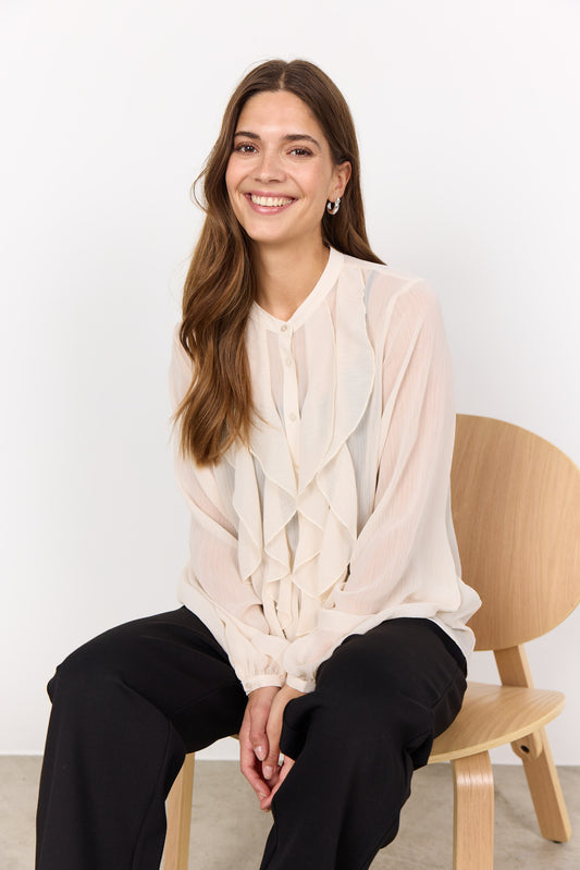 Woman sitting on a wooden chair wearing a light-colored blouse with a white background