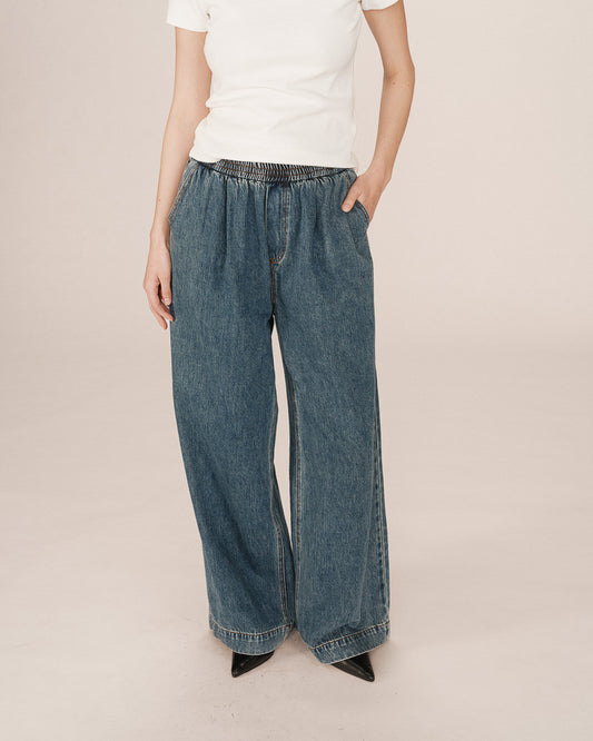 Person wearing blue wide-leg jeans and a white shirt on a beige background