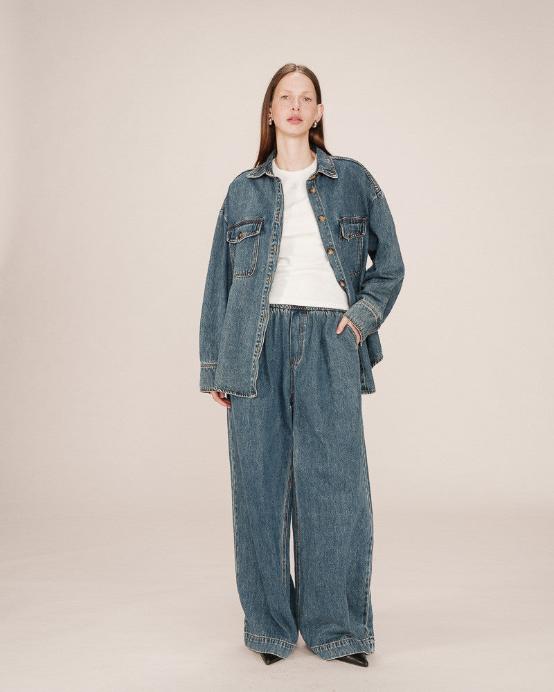 Person wearing a denim jacket and wide-leg jeans on a plain background