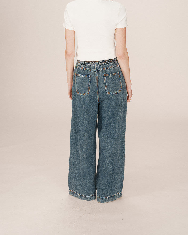 Person wearing blue jeans and a white shirt on a beige background