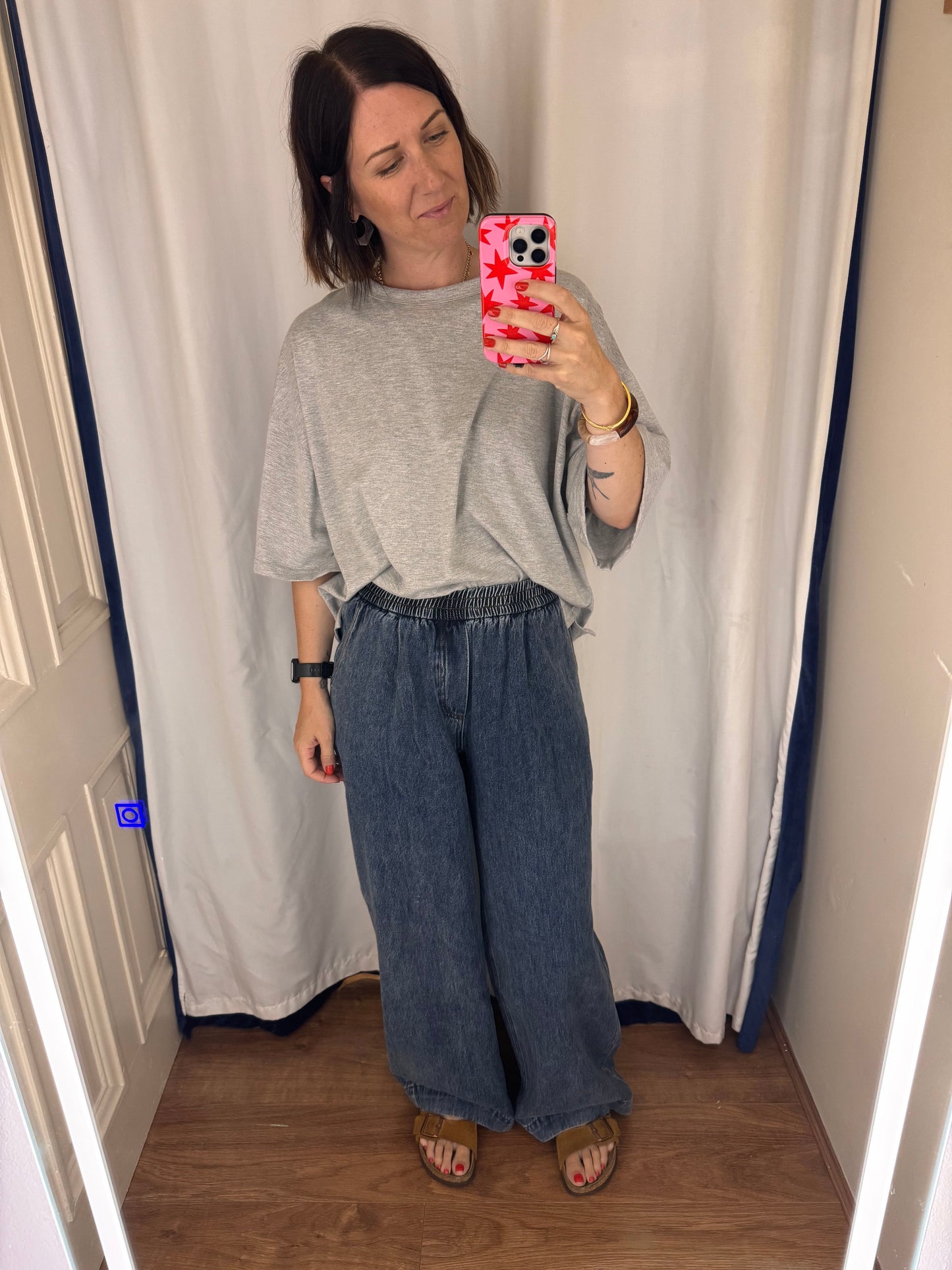 Person taking a mirror selfie in a room with a curtain and wooden floor.