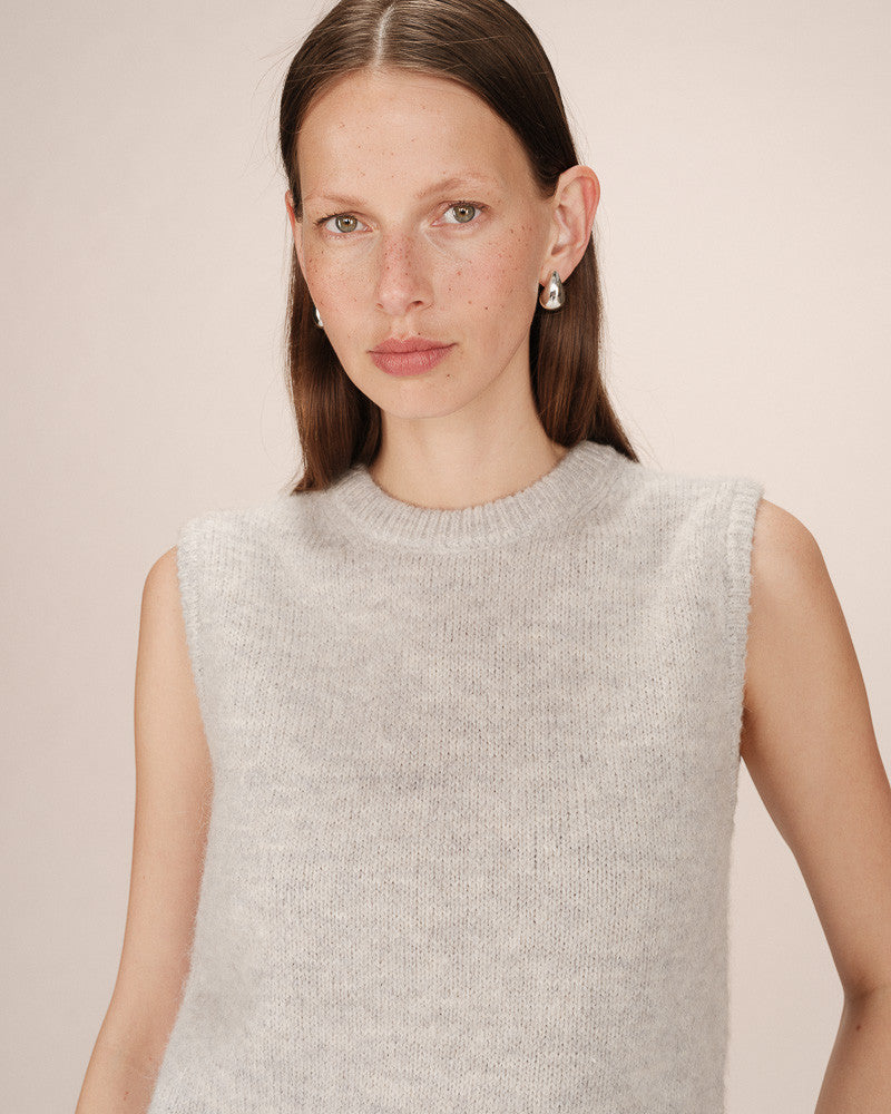 Woman wearing a light gray sleeveless sweater against a plain background