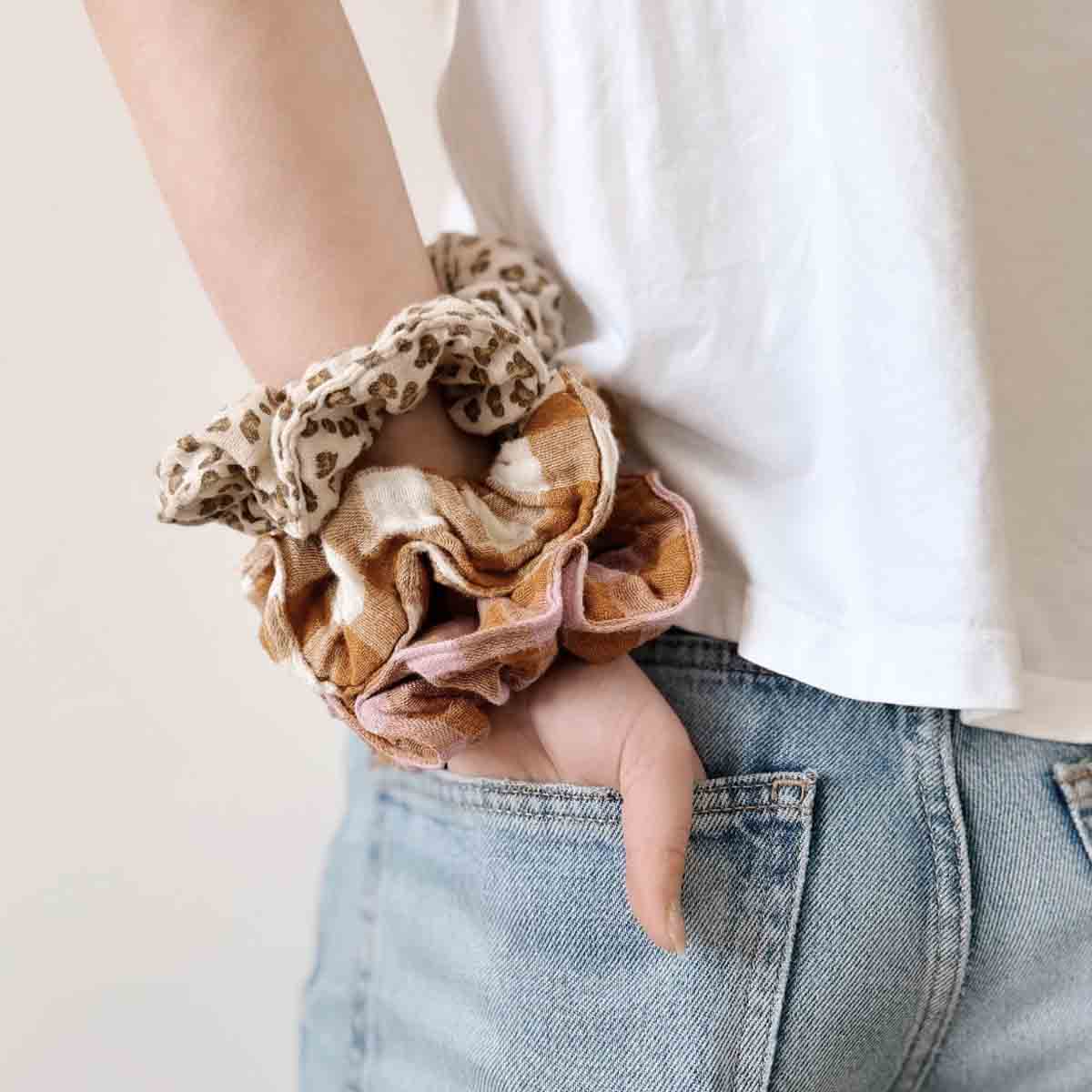 Person wearing colorful scrunchies on wrist with a neutral background