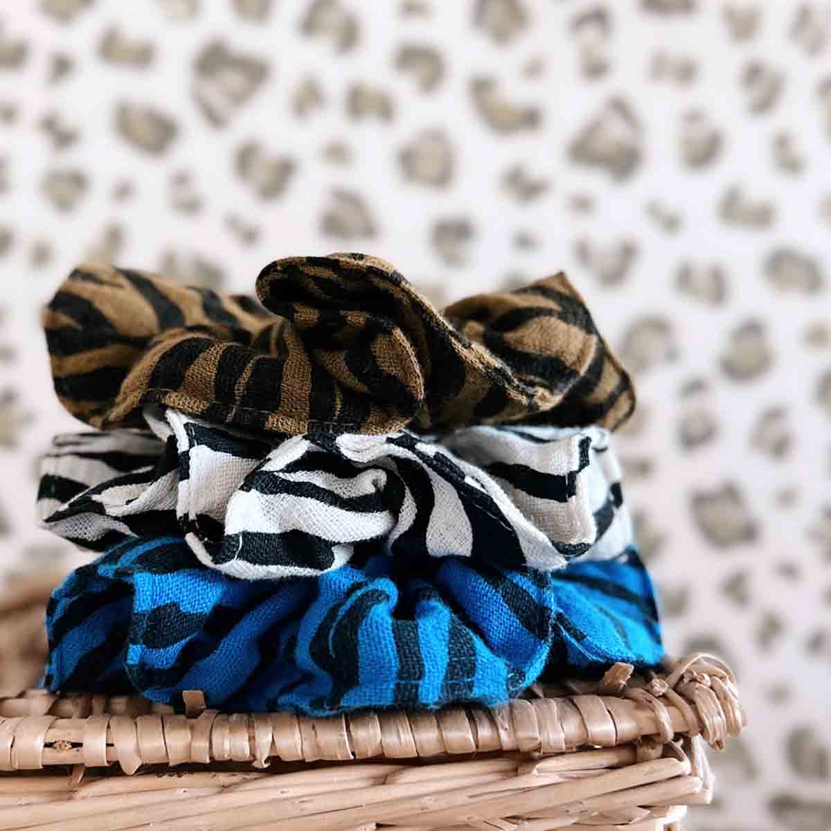 Three patterned scrunchies stacked on a woven surface with a textured background