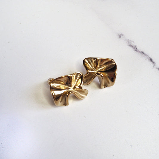 Pair of gold bow-shaped earrings on a marble surface