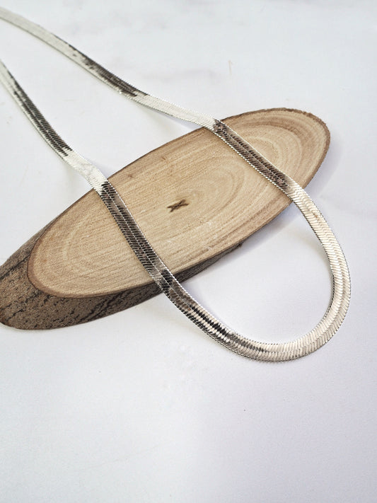 Silver snake chain on a wooden and white background
