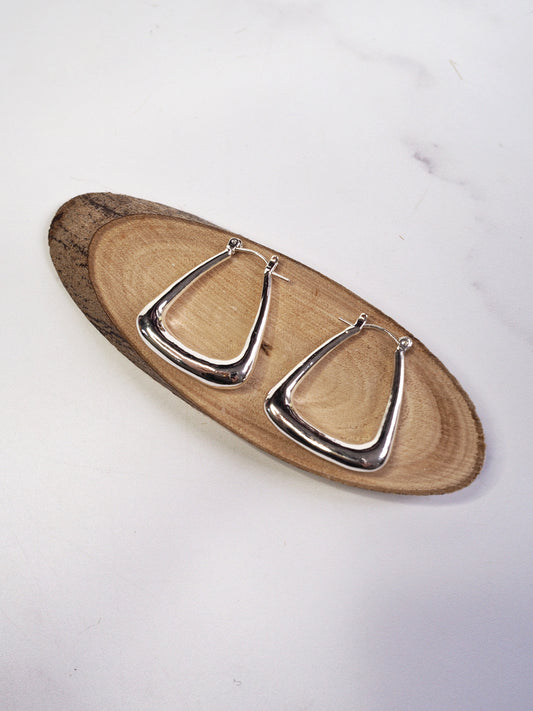 Pair of silver hoop earrings on a wooden tray with a white background