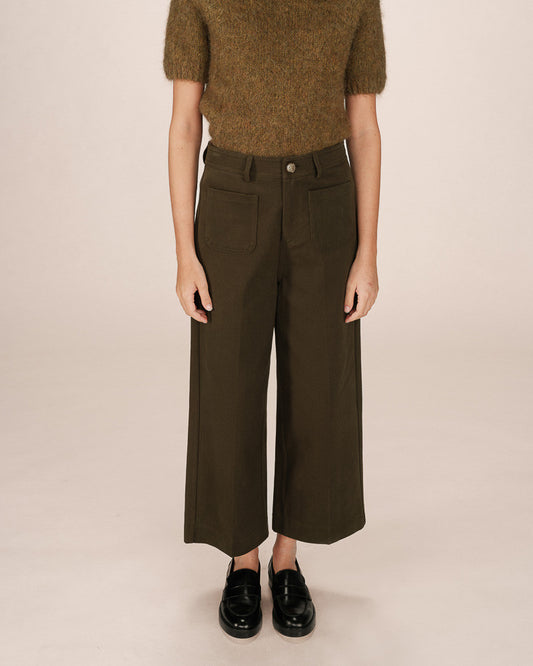 Person wearing a brown sweater and dark green wide-leg pants on a beige background