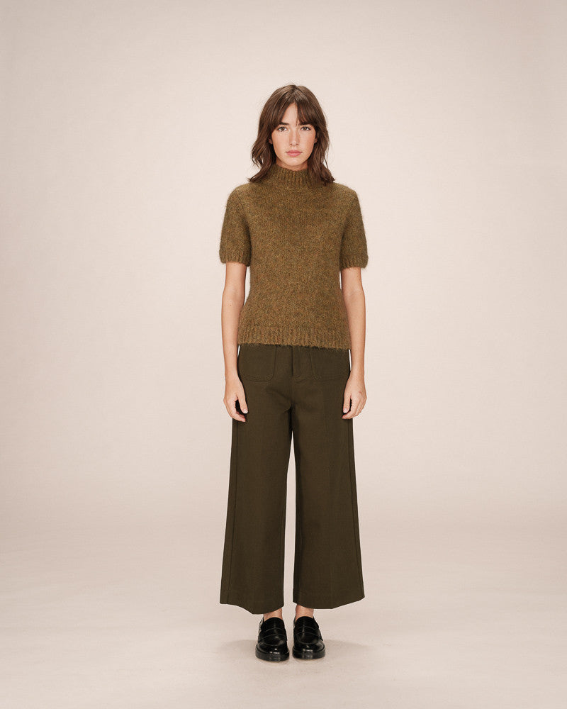 Woman wearing a green knitted sweater and dark green wide-leg pants on a beige background