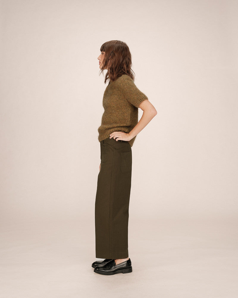 Person wearing a green sweater and dark green pants against a beige background