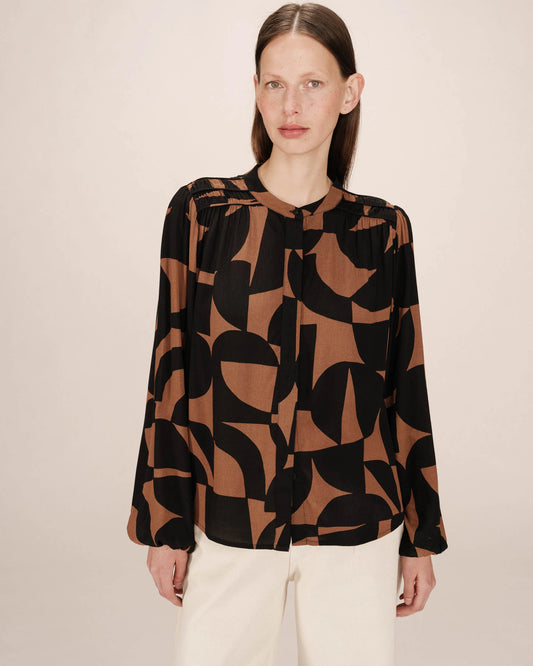 Woman wearing a brown and black patterned blouse against a beige background