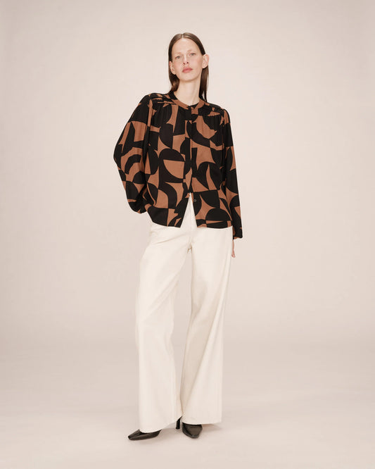 Woman wearing a patterned top and white pants on a plain background