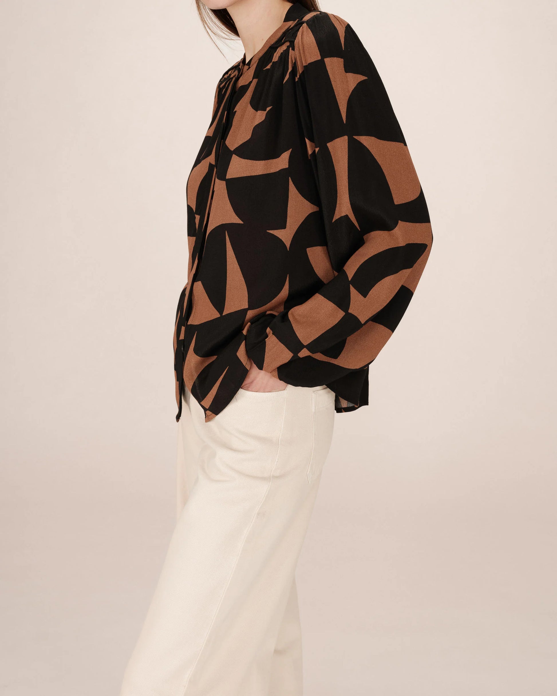 Person wearing a brown and black patterned top with white pants on a beige background