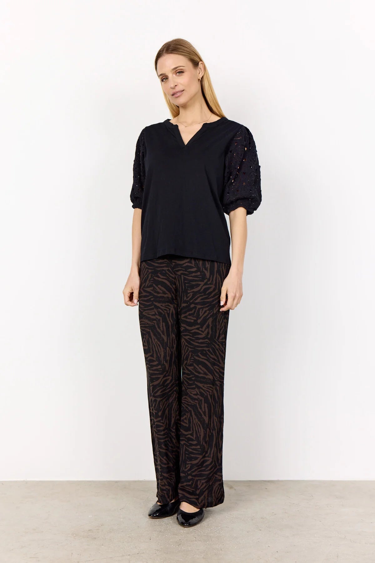 Woman wearing a black top and patterned pants against a white background