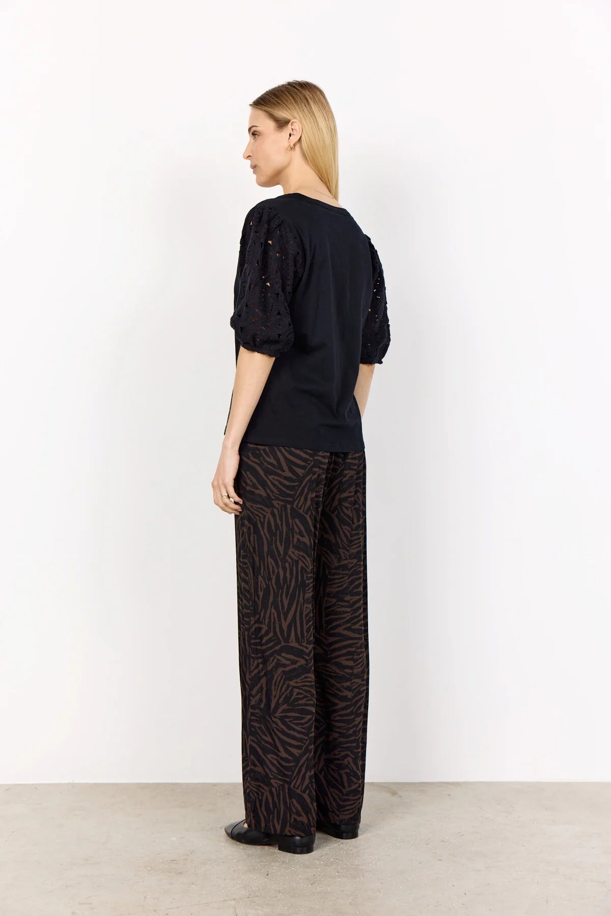 Woman wearing a black top and patterned pants against a white background
