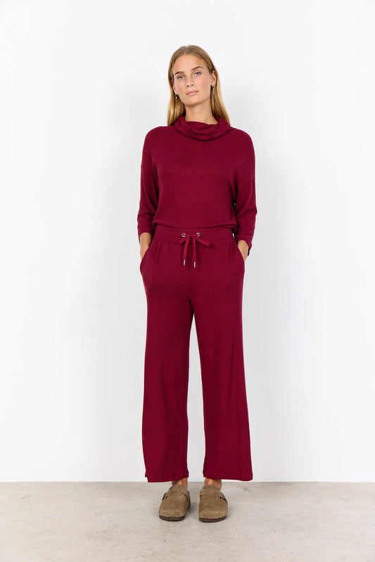 Woman wearing a burgundy outfit with a cowl neck top and wide-leg pants against a white background