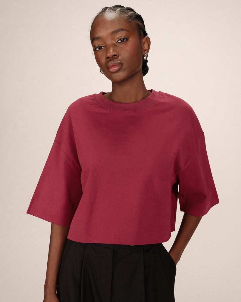 Person wearing a burgundy shirt and black pants on a beige background