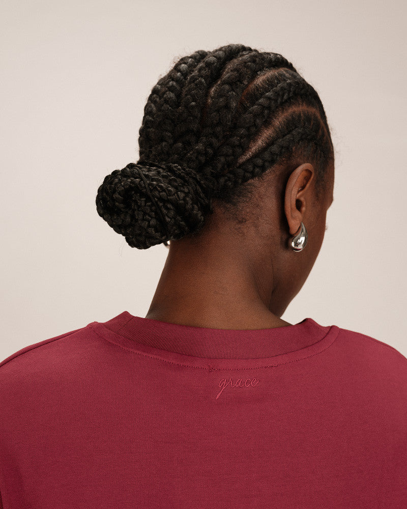 Person with braided hair wearing a red shirt on a beige background