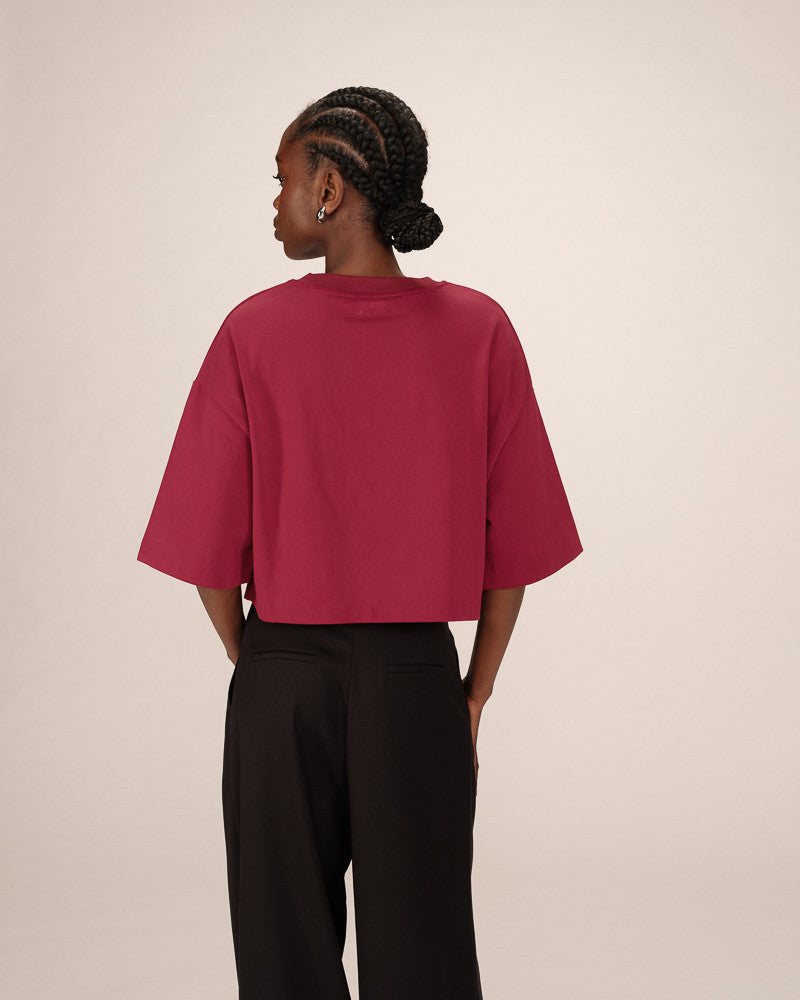 Person wearing a red oversized shirt and black pants on a beige background