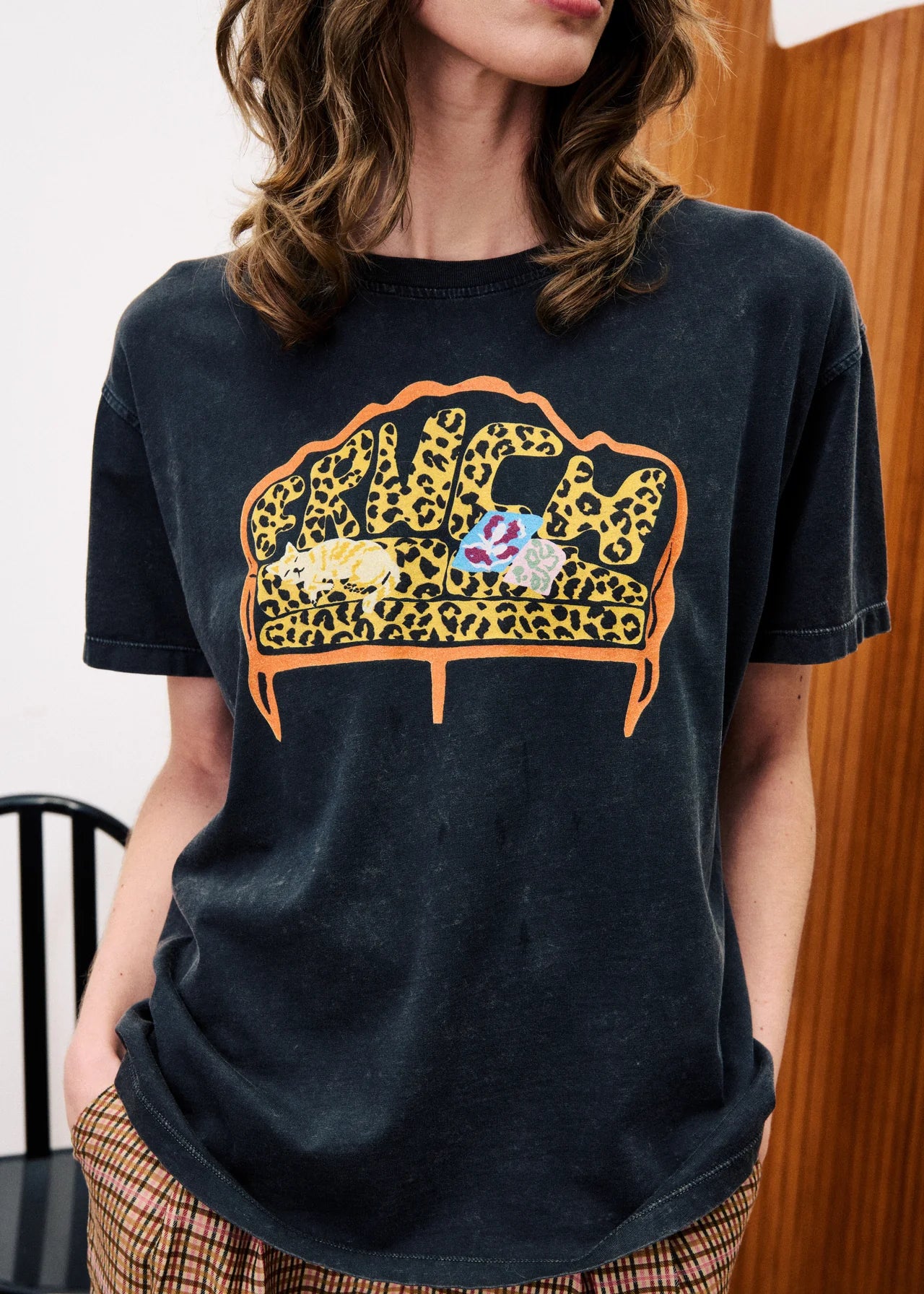 Person wearing a black t-shirt with a colorful graphic design of a couch.