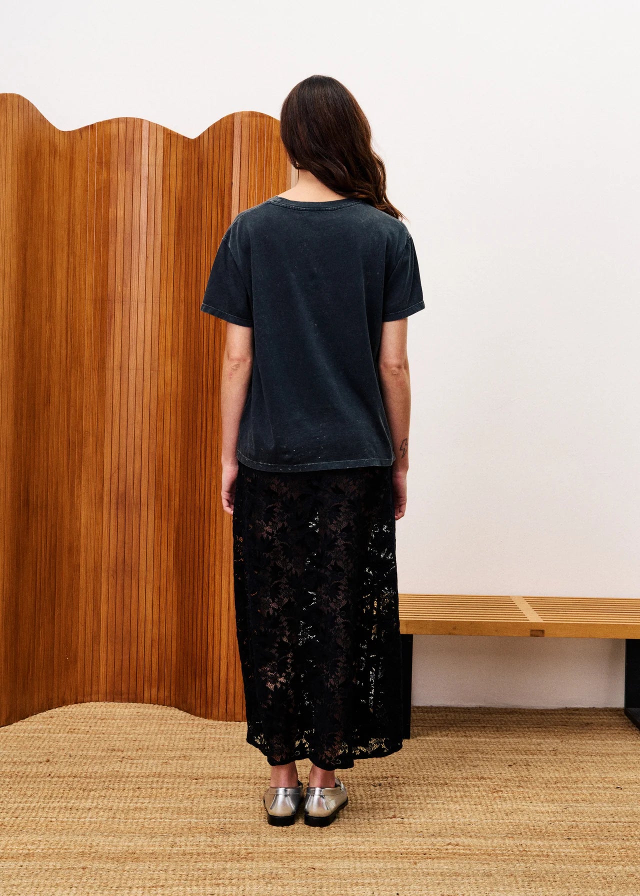 Person wearing a black t-shirt and black floral skirt standing in front of a wooden screen.