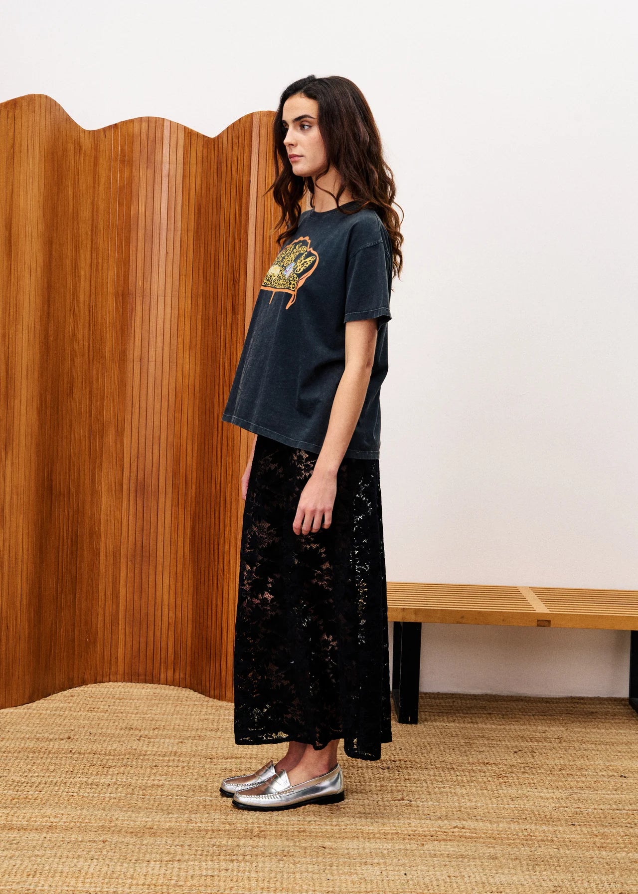 Woman wearing a dark blue t-shirt with a graphic design and black lace pants in a room with wooden paneling.