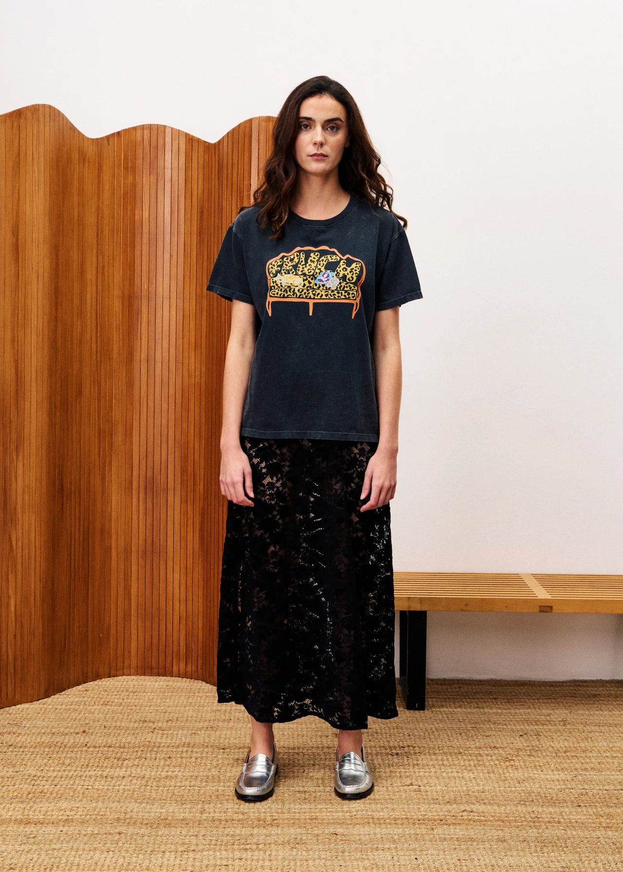 Woman wearing a black t-shirt with a graphic design in a room with wooden paneling and a bench.