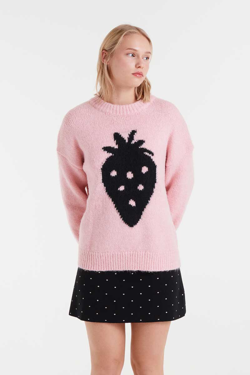 Woman wearing a pink sweater with a black design and a black polka dot skirt on a white background