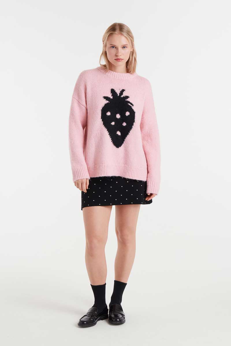 Person wearing a pink sweater with a black design and a black skirt on a white background