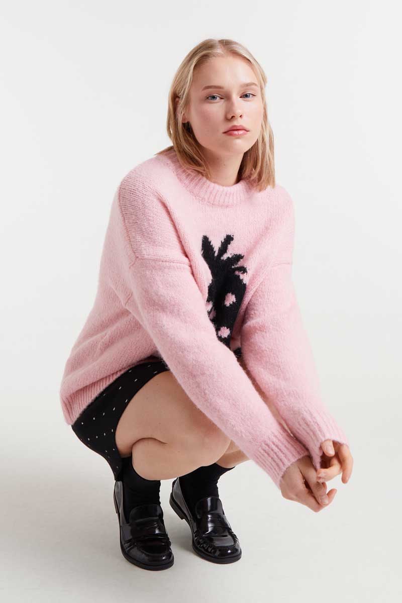 Woman wearing a pink sweater with black design on a white background