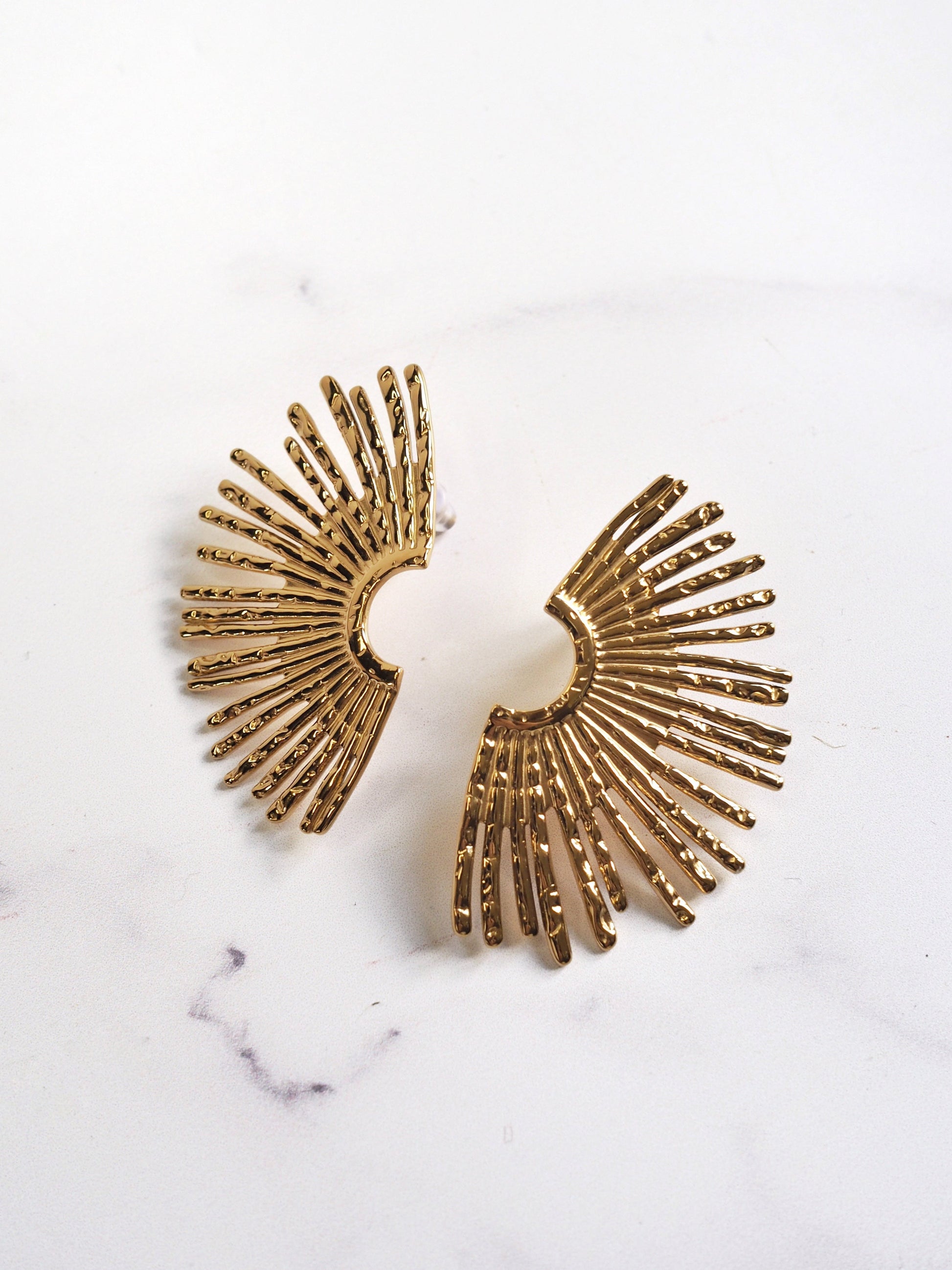 Gold sunburst earrings on a white marble background