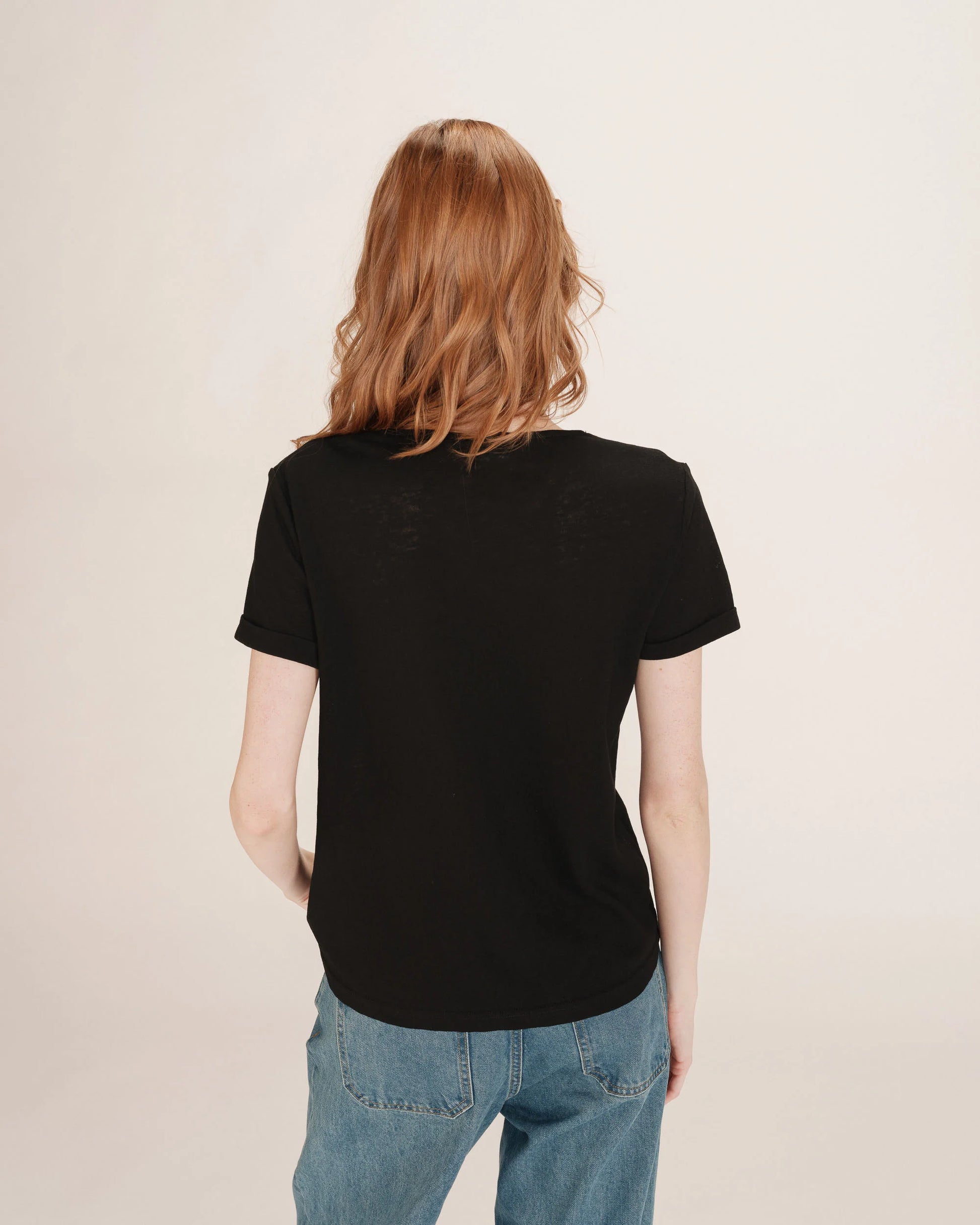 Person wearing a black t-shirt and blue jeans on a beige background