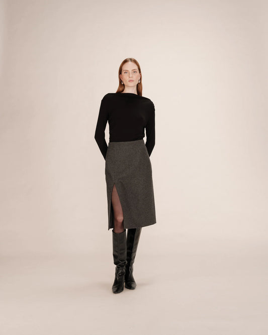 Woman wearing a black top and gray skirt with a slit on a beige background