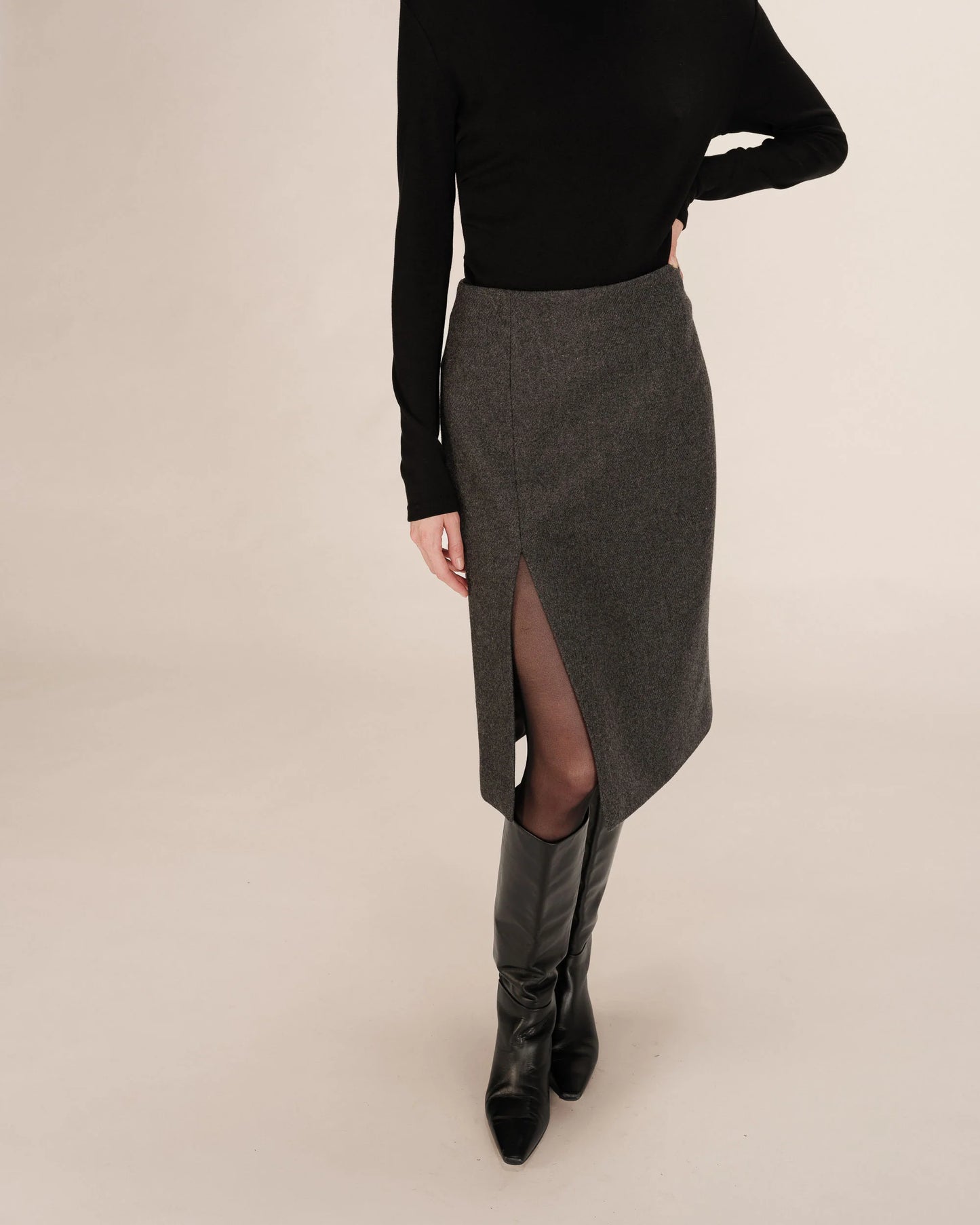 Person wearing a black top and gray skirt with a slit on a beige background