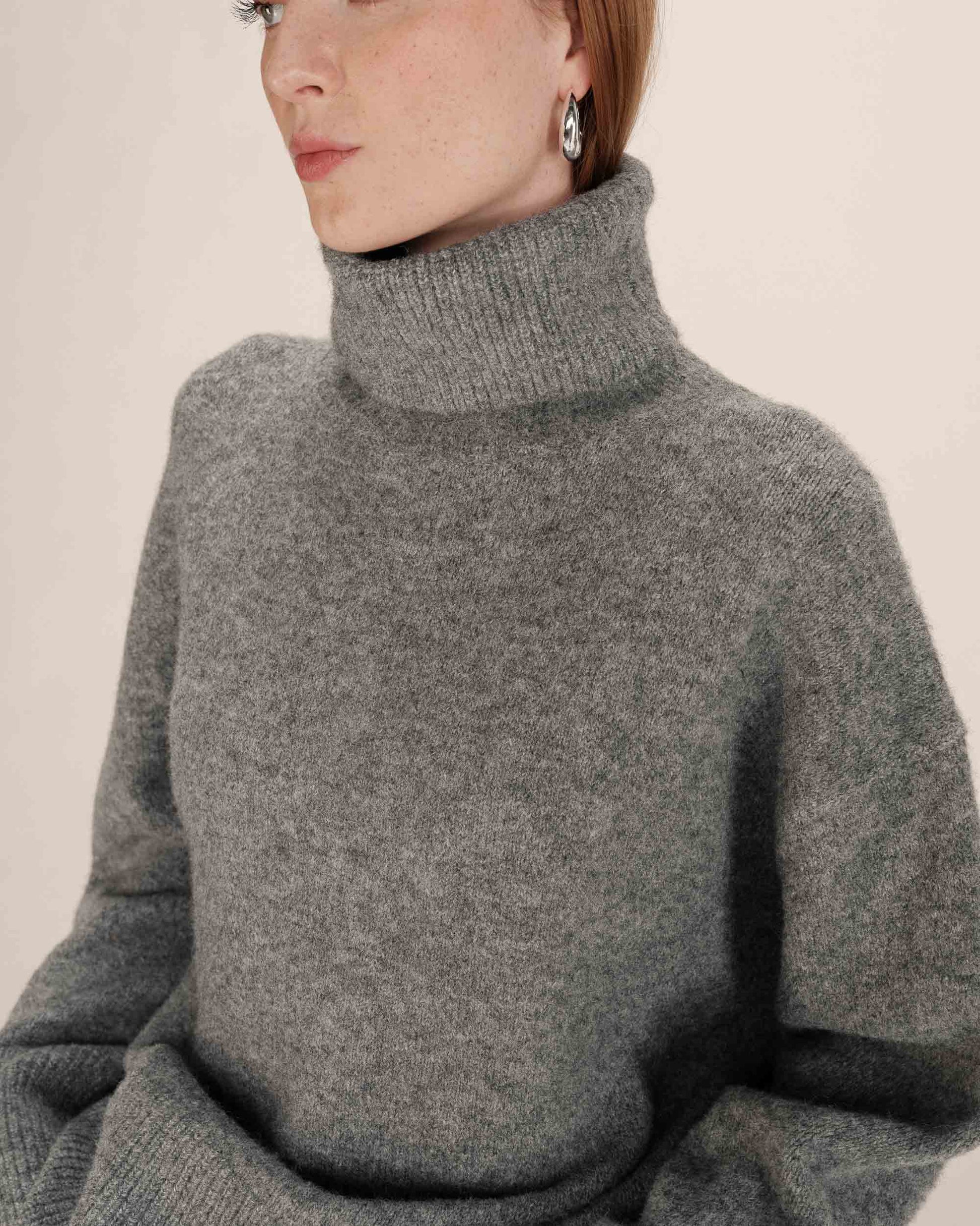 Person wearing a gray turtleneck sweater against a plain background
