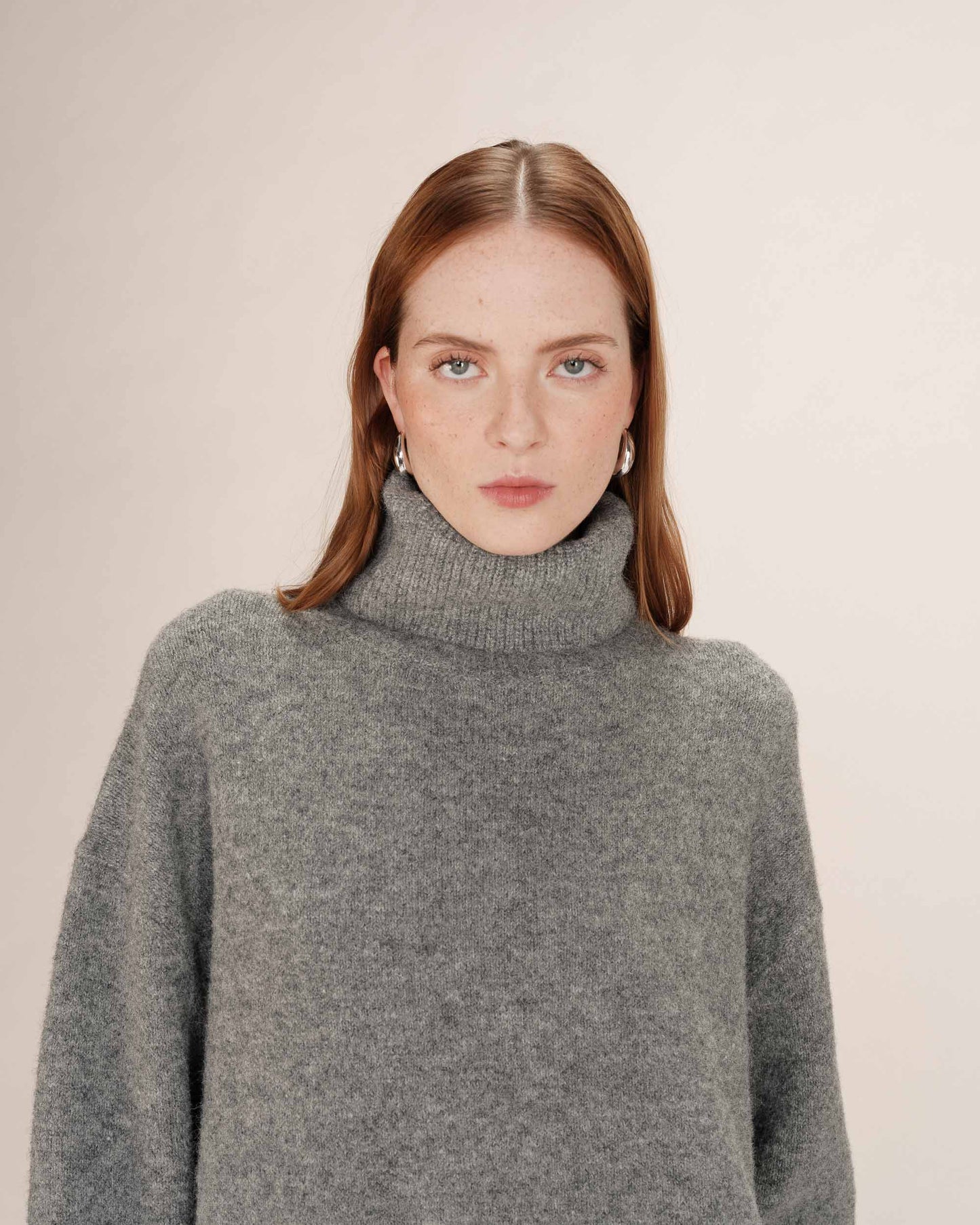 Woman wearing a gray turtleneck sweater against a plain background