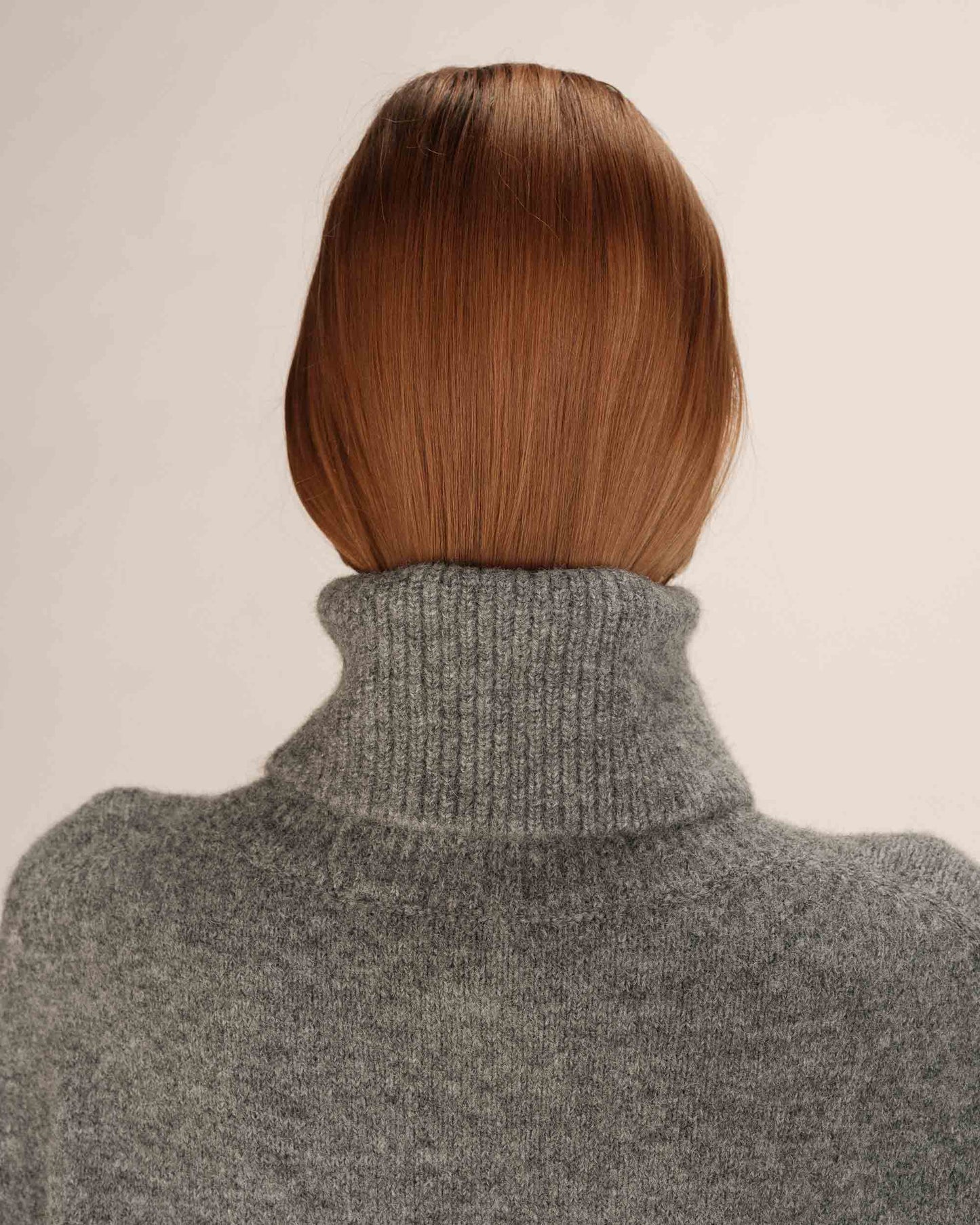 Person wearing a gray turtleneck sweater with a neutral background