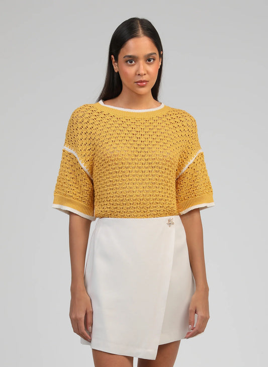 Woman wearing a yellow crochet top and white skirt on a gray background
