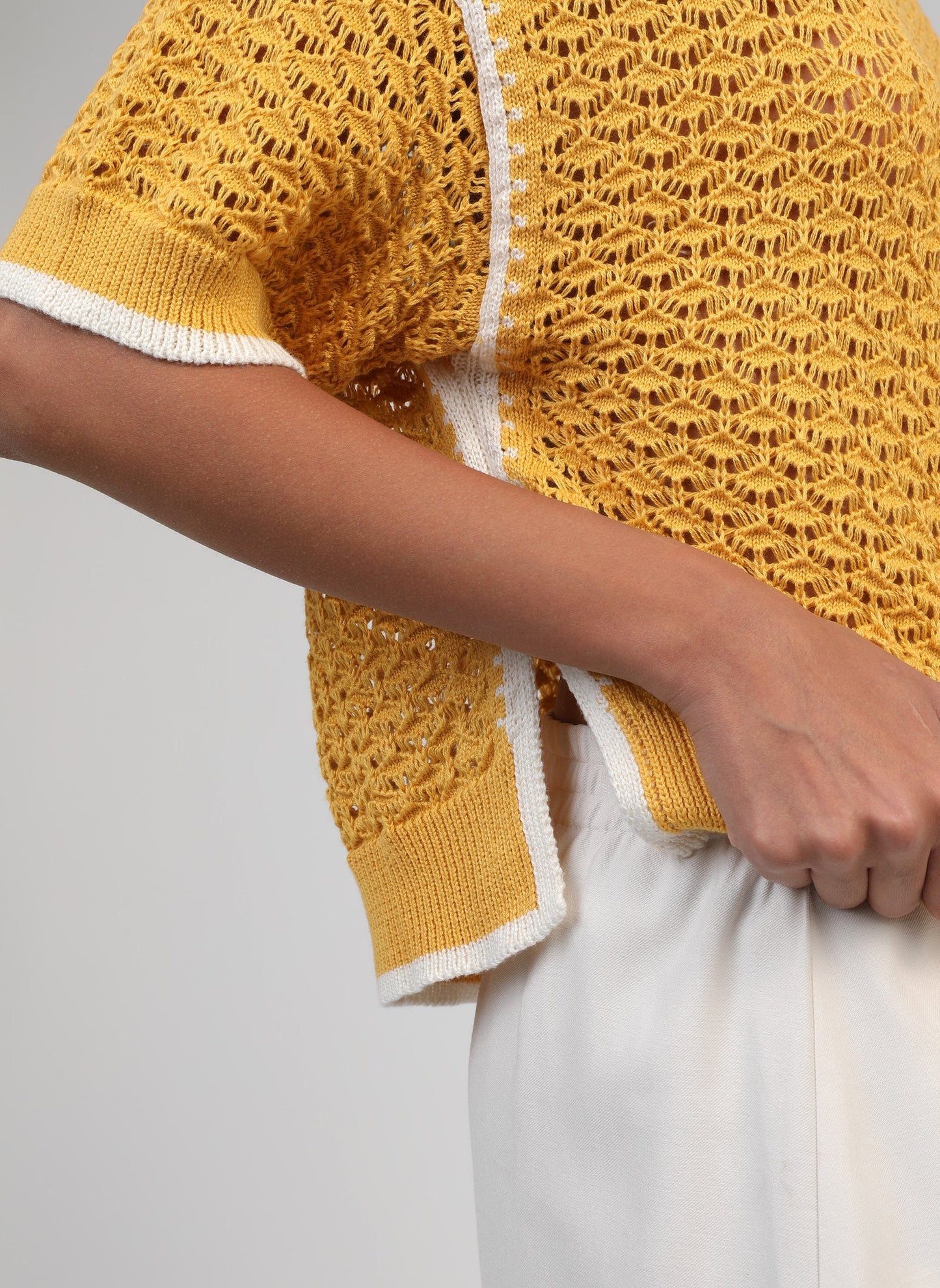 Yellow knitted cardigan with white trim worn by a person on a gray background
