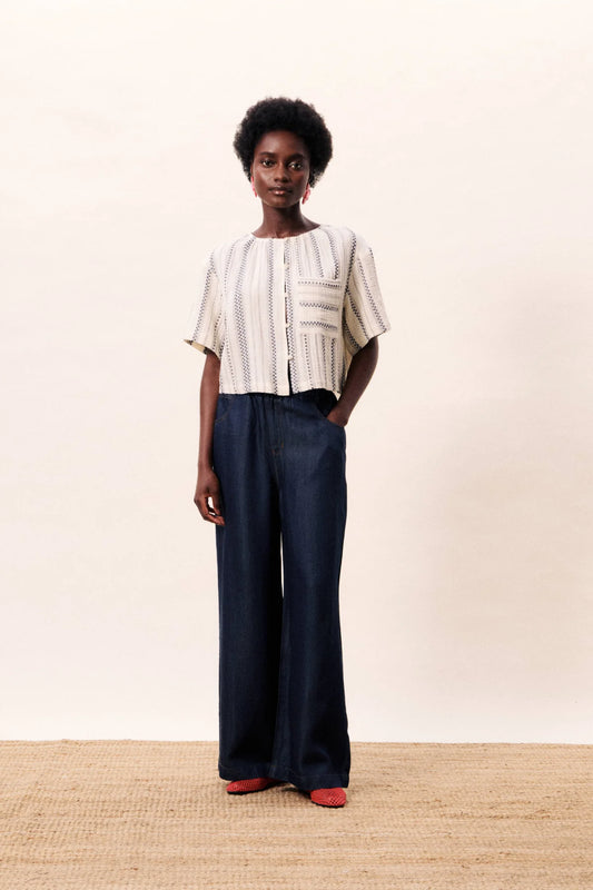 Woman wearing a beige top and dark blue pants against a plain background