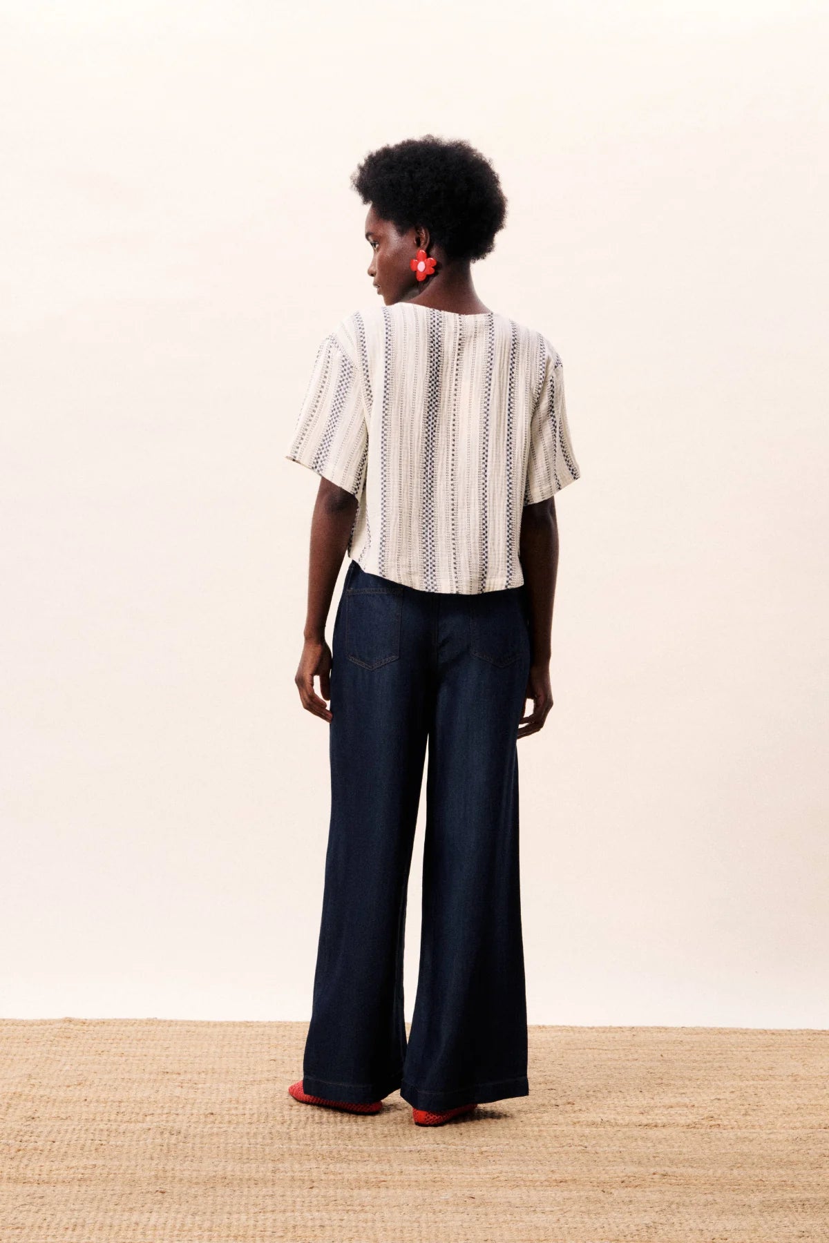 Person wearing a striped shirt and dark pants on a plain background