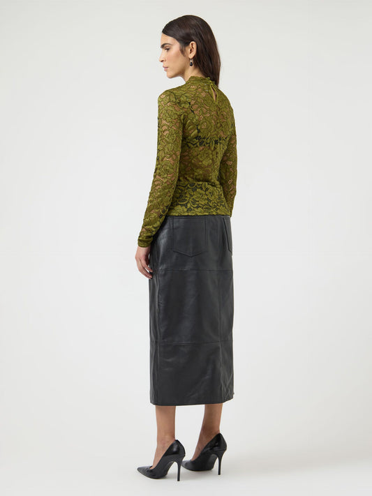 Woman wearing a green lace long sleeve top with a black leather skirt. Neutral background.