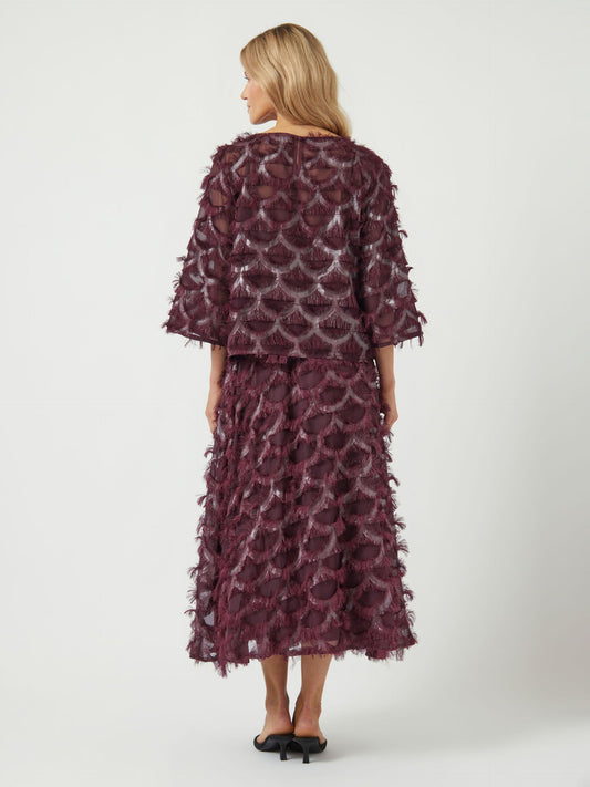 Woman wearing a burgundy patterned dress and top on a white background