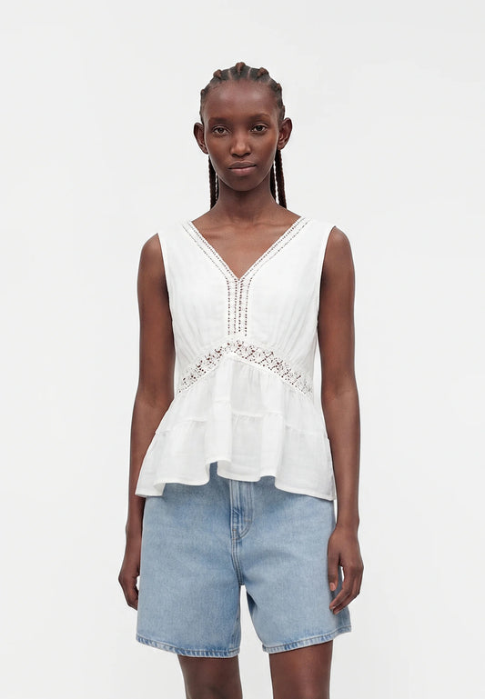 Woman wearing a white sleeveless top with lace details and light blue denim shorts on a white background
