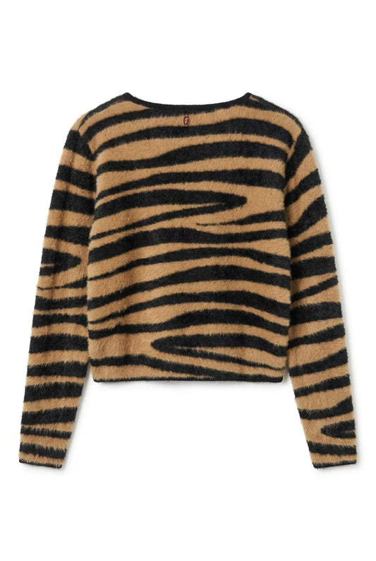 A fuzzy knit sweater with a bold black and tan zebra stripe pattern, hanging on a wooden hanger on a dark display table inside a clothing store.
